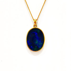 A 9ct yellow gold pendant with a large, oval-shaped triplet opal set in the center, showcasing vibrant blue and green hues. The pendant is displayed against a plain white background, emphasizing its colorful and glossy finish.